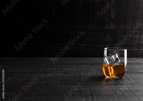 Glass of whiskey with ice on wooden background