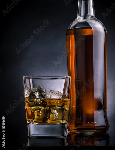 whisky-z-kostkami-lodu-w-szklanej-pobliskiej-butelce-na-czerni