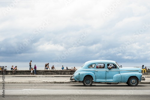 HAVANA, CUBA - MAY 18, 2011: Classic vintage American car serving as taxi drives along the seafront Malecon, a popular place for socializing in Central Havana.