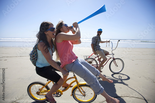 Poster Two women and one man riding bikes, having fun on the beach in San Diego, California