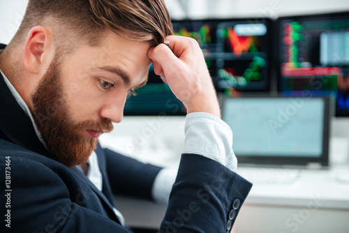 Poster Pensive bearded young businessman sitting and thinking in office