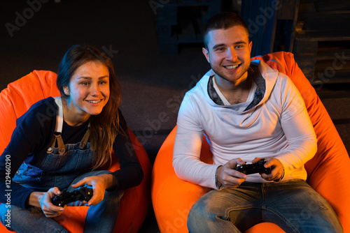 Poster Two young gamer sitting on poufs and playing video games togethe