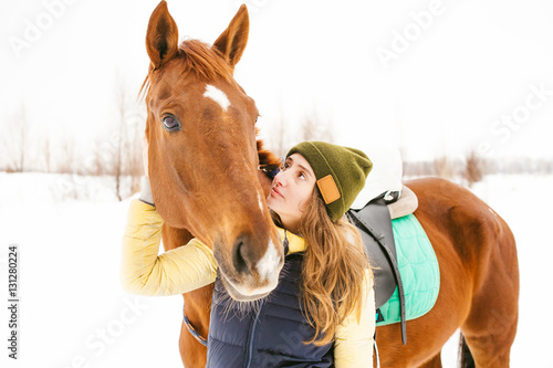 Female rider and horse in the open air. portrait of a beautiful young woman with her stallion, outdoors in winter. girl hugging and caressing the animal