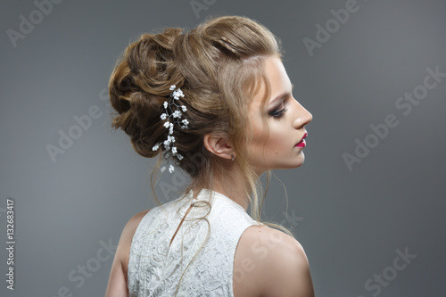 Elegant bride with a beautiful hairstyle and bright make-up isolated on a gray background. © ksi