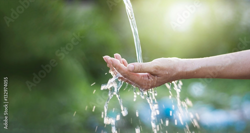 Water pouring in woman hand on nature background, environment concept © ipopba