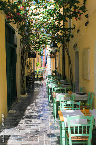 Poster Tables and chairs of cafe are on the narrow street of Rethymnon (part of Old Tow