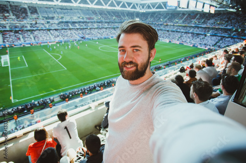 Poster Handsome bearded man watching football game and making selfie self-portrait with