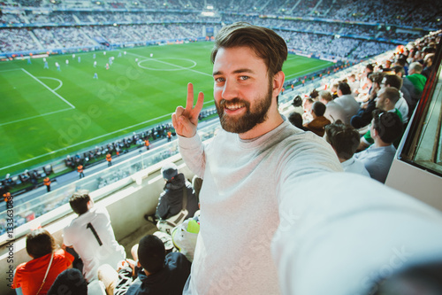 Poster Handsome bearded man watching football game and making selfie self-portrait with