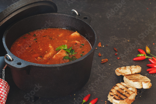Fish and tomato stew in cast iron pot with grilled bread slices on rustic table
