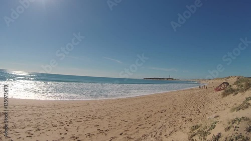 Unrecognizable people on the beach, with the Trafalgar lighthouse in the background, on the coast of Cadiz, Spain