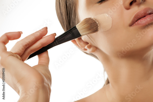 A young woman applied liquid foundation on her face with a brush