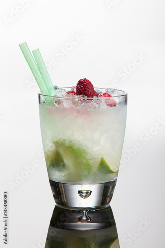 Raspberry vodka cocktail with lime sugar, raspberries and ice. On white background with reflection.