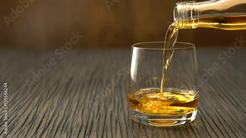 Pouring whiskey into the glass on a wooden table