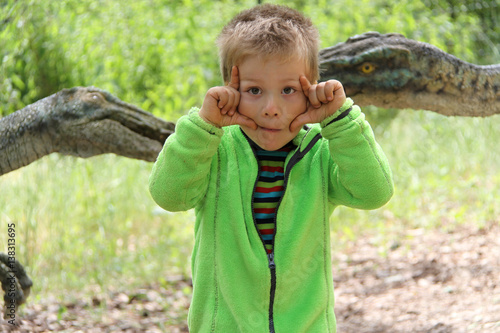 Poster Little boy with hands by his eyes with the dinosaurs in behind