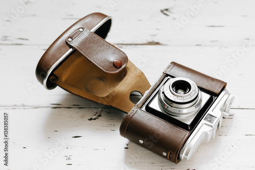 Old film camera in brown vintage case on white wood background