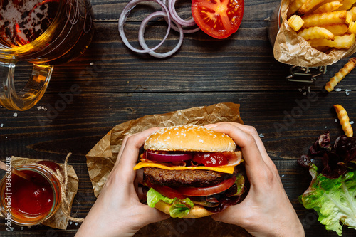 Poster Hands holding fresh delicious burgers with french fries, sauce and beer on the w
