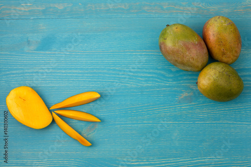 Three fresh mango and slices on a blue wooden background.