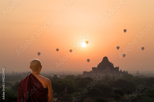 Poster Monk looking at hot air balloons at sunrise at Bagan temple in Burma, Myanmar