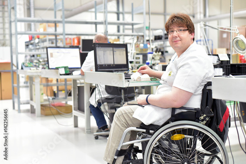 Rollstuhlfahrer am Arbeitsplatz in einer Fabrik zur Montage von Elektronik - Alltag mit Gehbehinderung // Wheelchair driver at the workplace in the industry © industrieblick