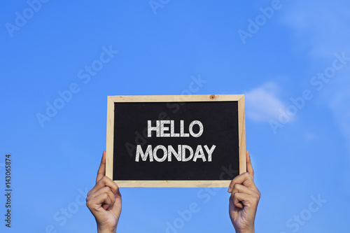 HELLO MONDAY/ Man holding small blackboard on blue sky background.