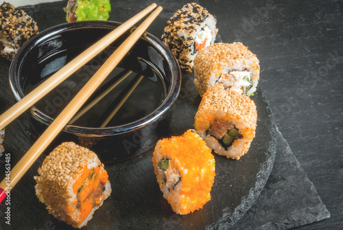 Concept of Japanese food: sticks and sushi, soy sauce and pickled ginger on a black slate stone table. Top view copy space