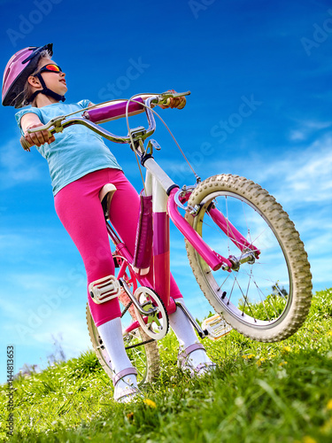 Child traveling bicycle in summer park. Children road bike for running on green grass. Bottom view aganist sky blue. Cycling trip is good for health.