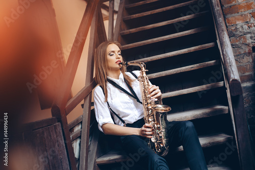 Obraz na plátně Playing young attractive girl sitting on steps with a saxophone outdoor