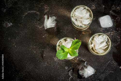 Alcohol cocktail made from golden tequila with ice cubes and mint. On a black concrete table. Copy space top view