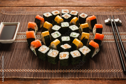 Bright colorful japanese sushi set, round ornament of maki rolls served on brown straw mat, closeup. Japanese food art, national cuisine, restaurant menu photo.
