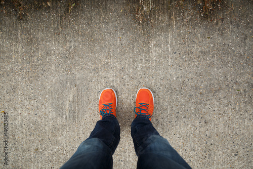 Man with orange shoes standing on a textured, concrete city street.