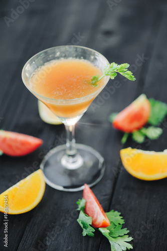 coctail with orange and tomato on black wooden table at blurred background