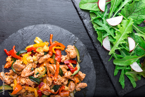 Poster Fry meat with vegetables near salad with arugula and radish on stone slate plates