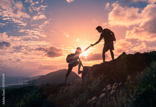 Team work, life goals and self improvement concept. Man helping his female climbing partner up a steep edge of a mountain.