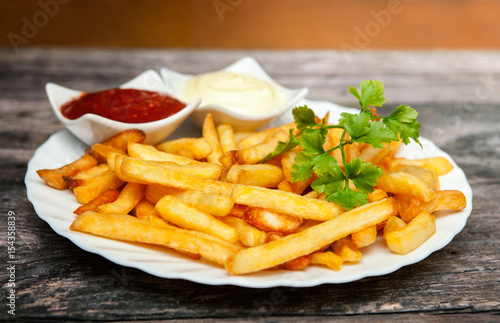 Poster French fries with tomato sauce, mayonnaise and parsley on wooden table