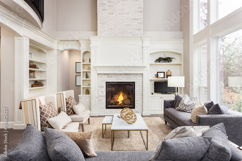 Beautiful Living Room in New Luxury Home with Fireplace and Roaring Fire. Large Bank of Windows Hints at Exterior View © bmak