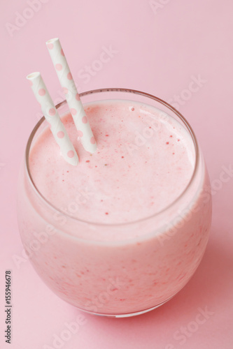 Strawberry pink smoothie in a glass with a straw on a pink background. Summer and healthy lifestyle concept.