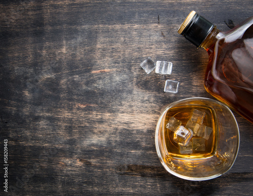 Glass with ice cubes and whiskey bottle on wooden table,top view
