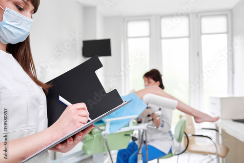 Cropped shot of a nurse writing on her clipboard professional gynecologist examining her patient on the gynecological chair on the background copyspace medicine gynecology health concept.