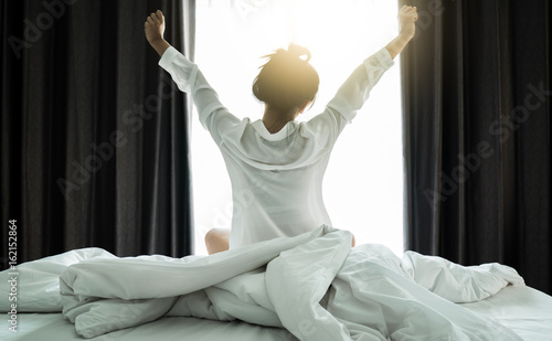 Asian women wake up from sleep. are stretch herself in the morning on the weekend sit on the bed at luxury room in Relax and weekend concept.