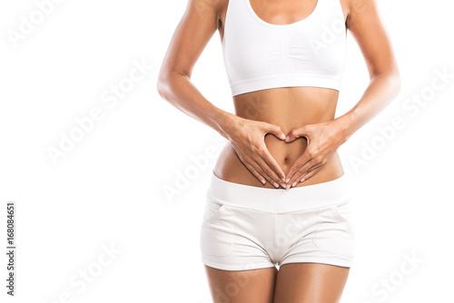 Fit young woman holding a heart over her abdomen, isolated on white background © Tijana