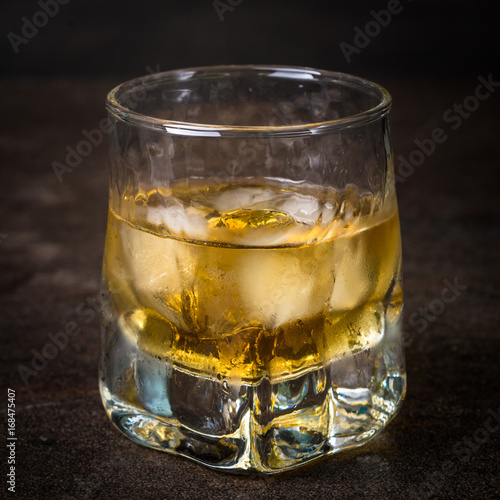 Whiskey with ice in glass on dark stone table.