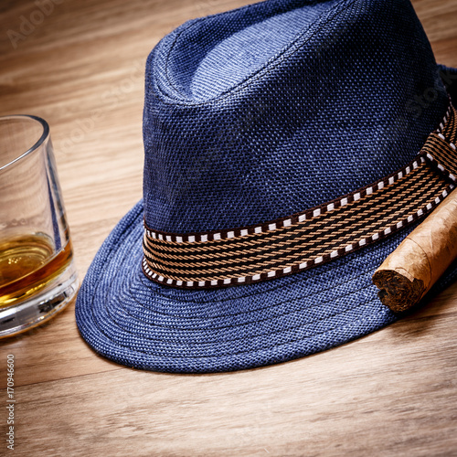 blue hat with cigar and expensive drink of whisky or rum on wooden floor