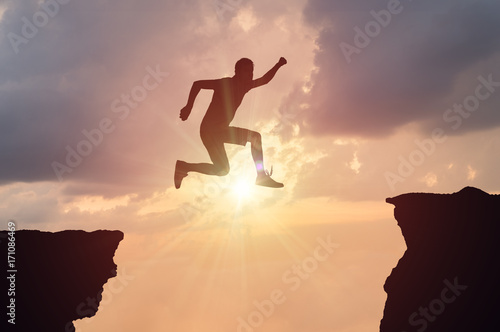Silhouette of man jumping over a gap at sunset.