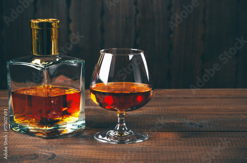 Glass of brandy or cognac and bottle on the wooden table.