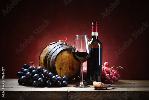 Red wine glass with bunches of grapes, bottle and small barrel