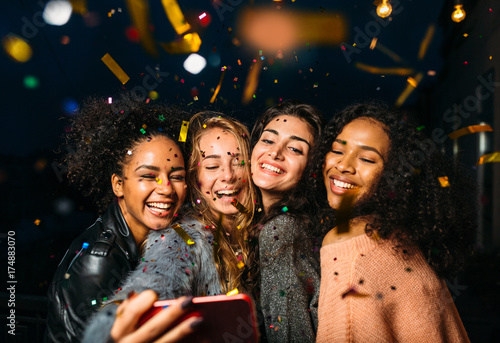 Group of happy women taking selfie on mobile phone, standing outdoors at night