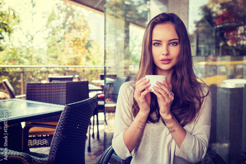 beautiful young girl sitting alone in a cafe drinks coffee