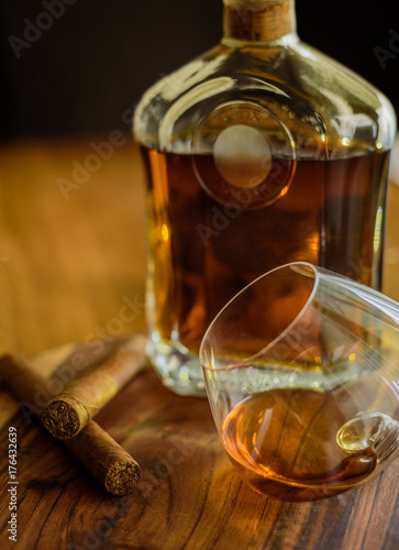 Close up of two cigars, a glass and a bottle of rum on a wooden surface