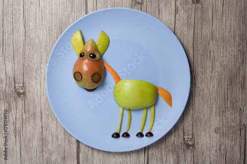 Horse made with apple and pear on plate and wooden texture