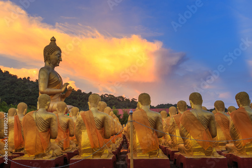 Big golden buddha statue and many small golden buddha statues sitting in row at at Buddha Memorial park, Nakornnayok Thailand.